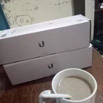 Two boxed access points on a desk beside a cup of coffee