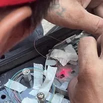 Hands splicing fiber in a closure, a red test light showing through