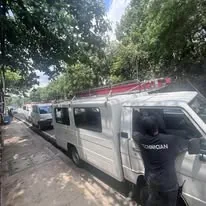 A technician at the door of the white service van, a ladder on its roof